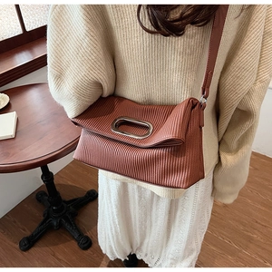 Detailed view of brown pleated texture handbag with silver oval metal handle and strap