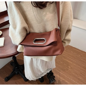 Detail of brick red pleated shoulder bag with oval silver metal handle and texture
