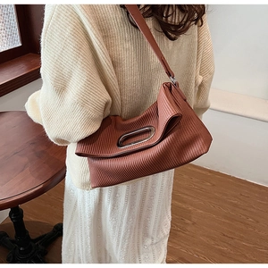 Detail of a brown pleated shoulder bag with vertical texture and silver metal handle