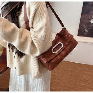 Detail of a brown pleated shoulder bag featuring a decorative silver oval metal buckle