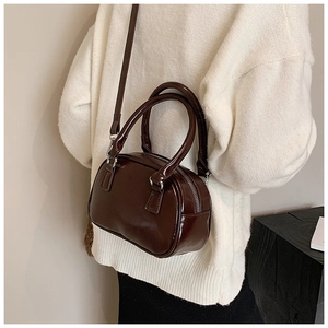 Close-up of a glossy dark brown leather bowling bag with metallic zipper and shoulder strap