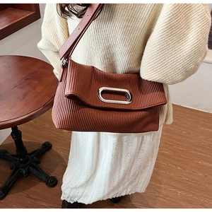 Close-up of brown pleated leather crossbody bag with oval metal buckle detail
