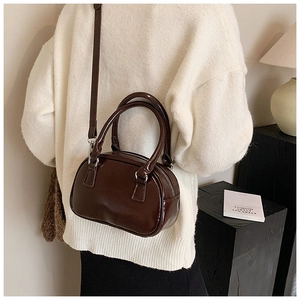 Detail view of a chocolate brown glossy crossbody bag worn over a beige coat
