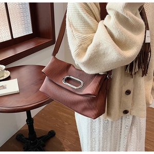 Detailed close-up of brown pleated leather shoulder bag with oval silver metal buckle