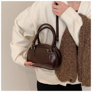 Detail of dark brown glossy cylinder bag with double handles and silver zip hardware