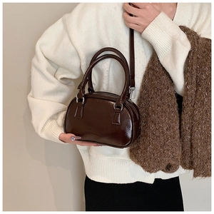 Detail of a chocolate brown glossy PU leather Boston bag with round handles and strap