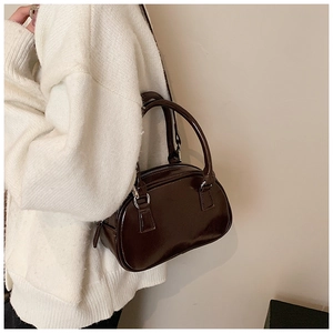 Detail of dark brown patent leather bowling bag with silver hardware on a white knit sweater