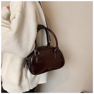 Close-up of deep brown glossy bowling bag featuring silver hardware on a white knit cardigan