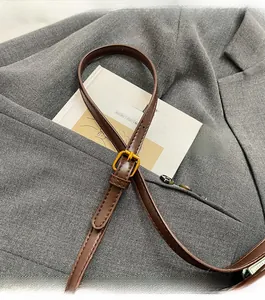 Detail of adjustable brown leather shoulder strap with gold buckle on a grey suit