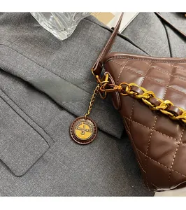 Macro detail of brown quilted leather bag with shiny gold chain and round metallic charm