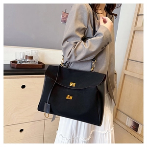 Close-up of matte black leather bag with gold locks on a model in a minimalist setting