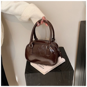 Detail of a dark brown glossy patent leather bowling bag with silver metal ring connectors