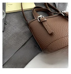 Détail du sac seau en cuir marron à motif litchi avec boucle argentée et coutures fines