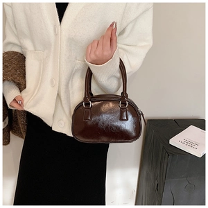 Detail of a shiny dark brown cylindrical handbag with silver metal rings and chic design