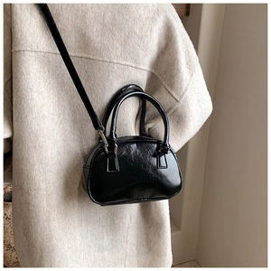 Detail of a black glossy leather mini crossbody bag worn with a beige wool coat