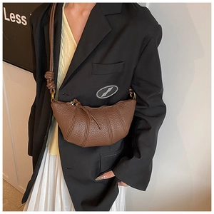 Close-up of a brown pebble leather croissant bag showing textured pleats and crossbody strap