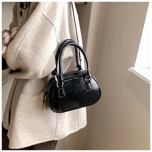 Detail of a shiny black bowling bag with silver hardware on a model outfit