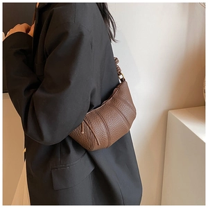Detail view of dark brown pebbled leather crescent bag worn over a black blazer