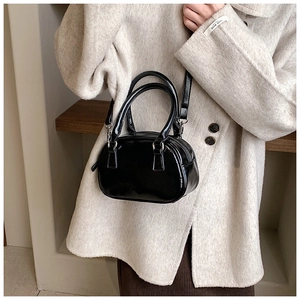Model wearing a black glossy patent leather mini bowling bag with silver hardware