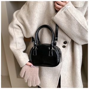 Detail of glossy black patent leather mini bowling bag held by a model in beige coat