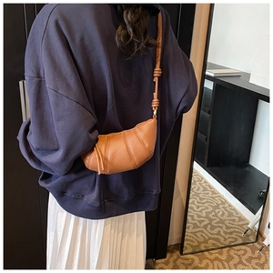 Detail of dark caramel croissant bag with knotted leather strap and curved stitching