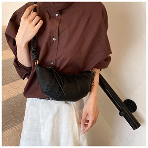 Detail of black pebbled leather croissant bag with pleated stitching worn by a model