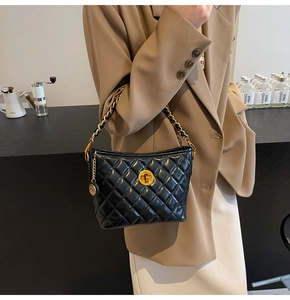 Detail of black quilted chain bag with gold twist lock and woven strap on a table