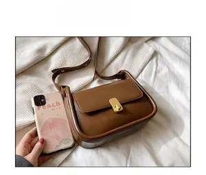 Size comparison of a caramel brown leather shoulder bag with a gold buckle and a smartphone