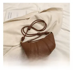 Detail of brown lychee texture leather crescent bag with knot strap on soft blanket
