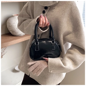 Detail of a black patent leather bowling bag held by a model in a beige wool coat