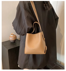 Detail of caramel lychee textured bucket bag featuring embossed logo and wide strap