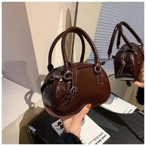 Close-up of a glossy dark brown mini bowling bag with dual handles and silver hardware
