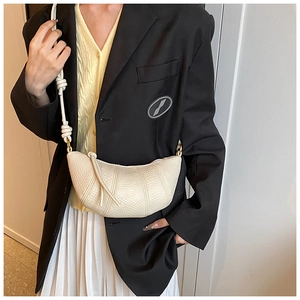 Detail of a creamy white crescent bag with pebble texture and thick rope shoulder strap