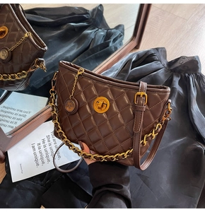Detail of a brown quilted leather bag with gold chain and circular metal pendant charm