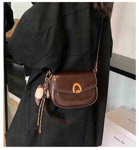 Detail der braunen Satteltasche mit goldenem Metallverschluss und dekorativem Bommel-Anhänger