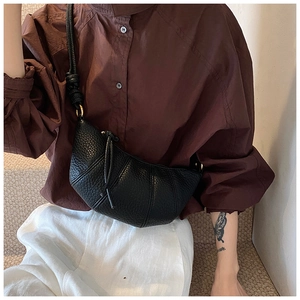 Detail of black lychee grain leather croissant bag with pleated texture and gold hardware