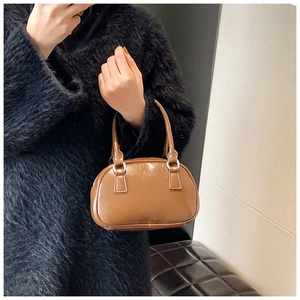 Close-up of brown glossy leather handbag with silver rings and fine stitching detail