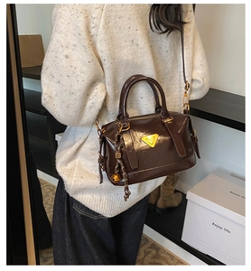 Detail view of dark brown glossy leather handbag with golden logo and bell charm