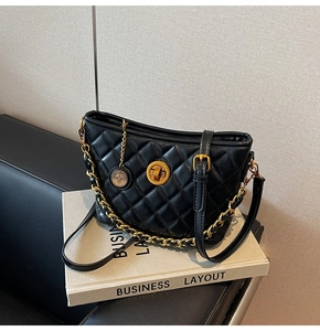 Detail of black quilted chain bag with gold hardware and logo pendant on a book