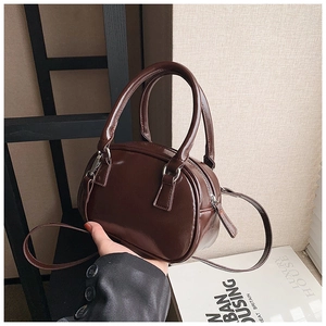Detail of a dark brown mini Boston bag in glossy patent leather with adjustable strap