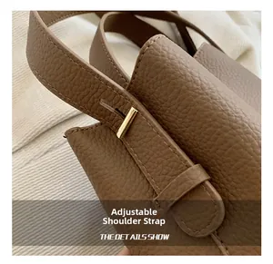 Detail view of adjustable shoulder strap with gold buckle on brown lychee leather bag