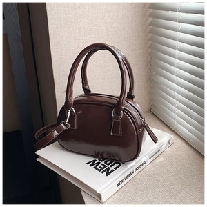 Detailed view of deep brown glossy small Boston bag with double handles on white books