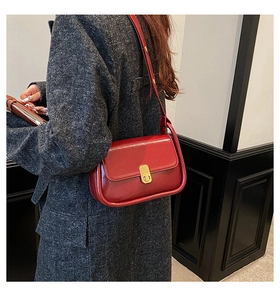 Detail of a dark red glossy leather crossbody bag with a gold buckle on a grey coat