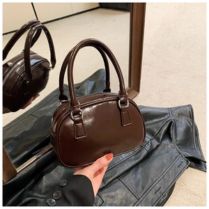 Detail of a dark brown glossy patent leather bowling handbag with metallic zipper