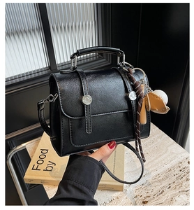 Close-up of black glossy leather satchel with baseball charms and metal buckle detail