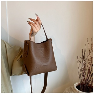 Close-up of brown bucket bag showing lychee grain leather texture and MACGNEE logo detail
