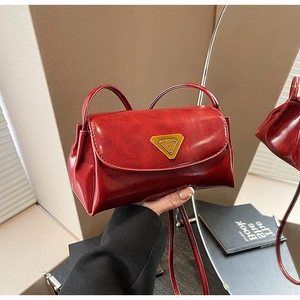Detailed view of dark red leather crossbody bag with triangular gold metal logo clasp