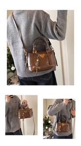 Detail of a dark brown patent leather boston bag featuring a triangle metal plate and strap