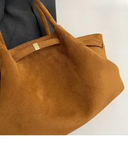 Gros plan sur la texture en daim marron et la boucle en métal doré d'un sac cabas d'épaule