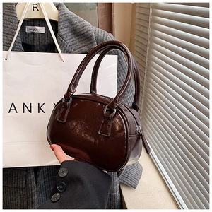 Detail of a dark brown mini glossy bowling bag with shiny faux leather texture and handles